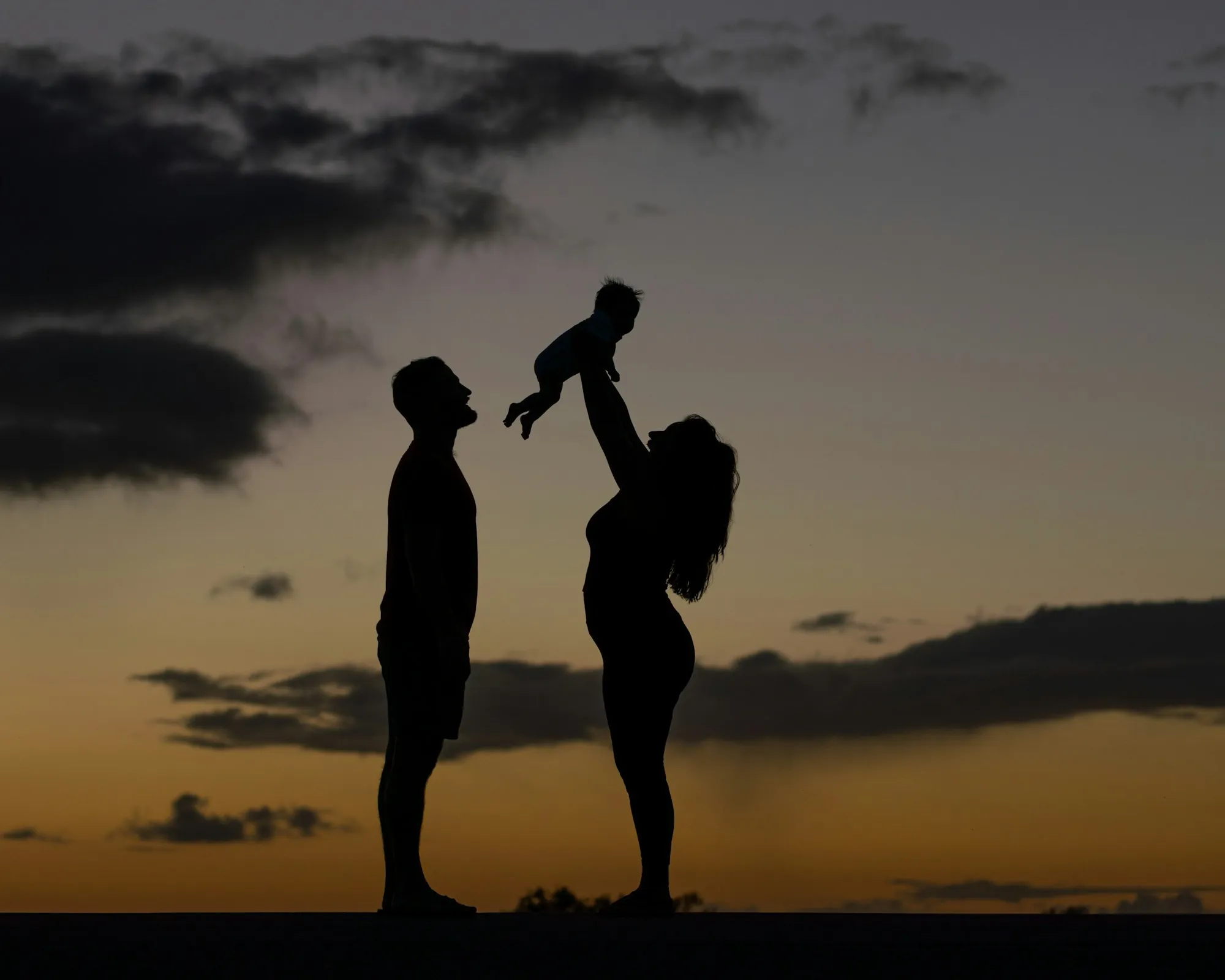 Silhouette of parents lifting their child at sunset
