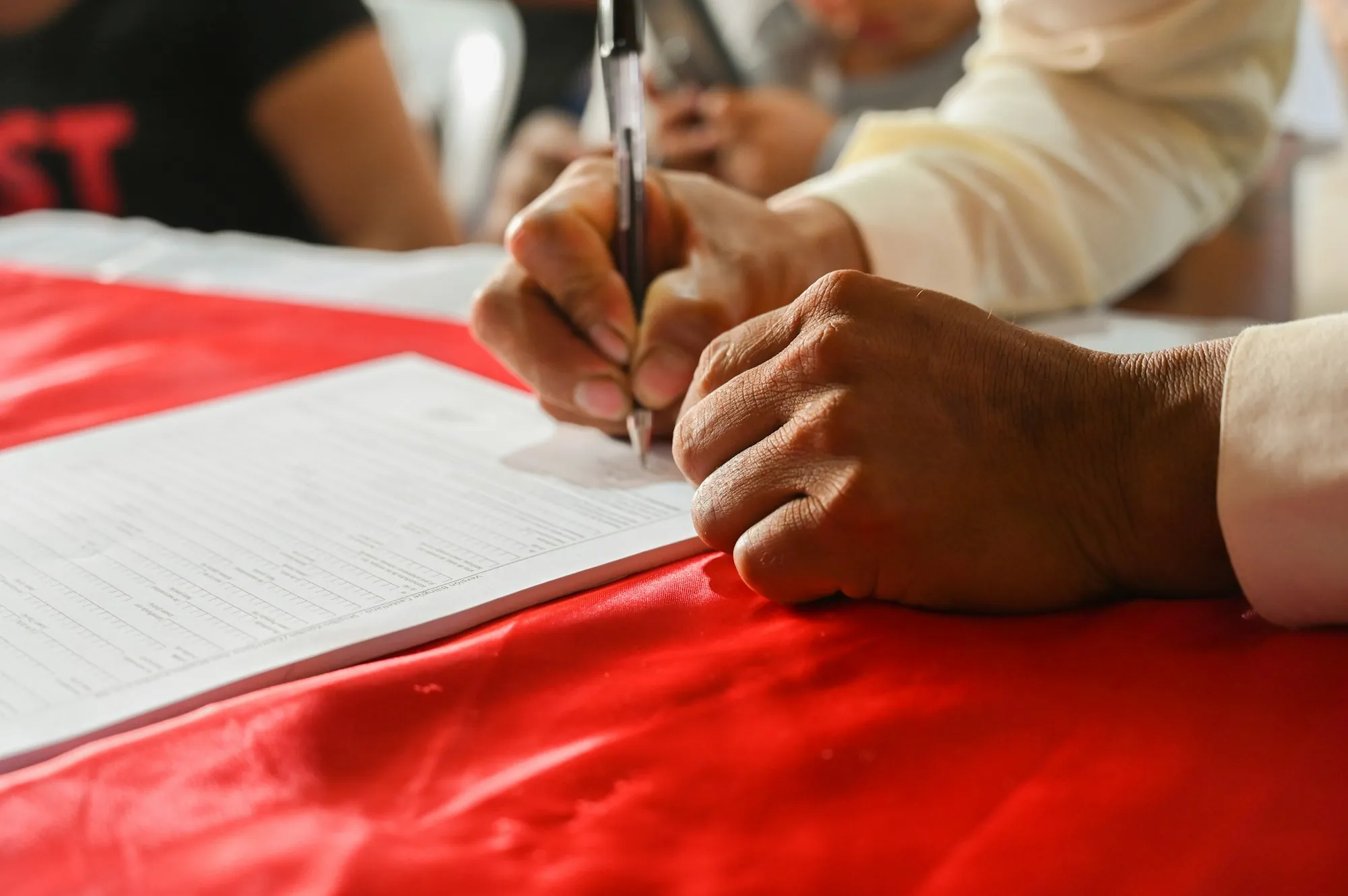 Hands signing a document on a red tablecloth